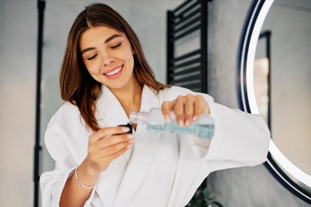 Chica en el baño con bata usando colutorio o enjuague bucal por su higiene bucal